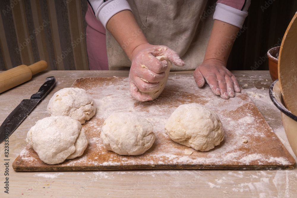A woman kneads the dough. Plywood cutting board, wooden flour sieve and wooden rolling pin - tools for making dough. A woman kneads the dough. Plywood cutting board, wooden flour sieve and wooden rolling pin - tools for making dough.