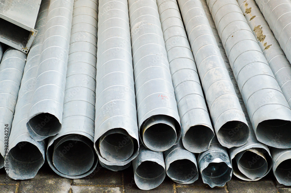 Fototapeta premium Large iron metal tin corrugated ventilation pipes of large diameter for the industrial construction of ventilation at a construction site during the repair