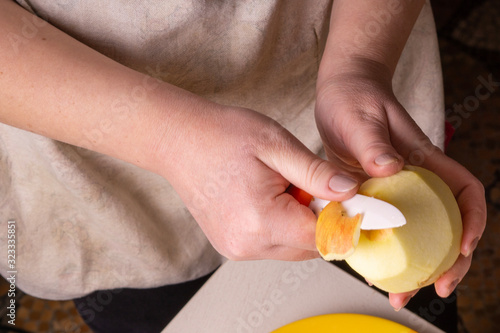 Hands of an elderly woman peeling an apple with a white ceramic knife.