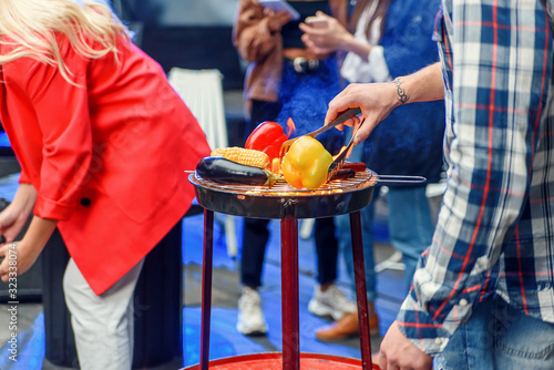 Handsome man is grilling delicious food on grill for his friends at barbecue party outdoors. Picnic time, weekend. Slow motion photo