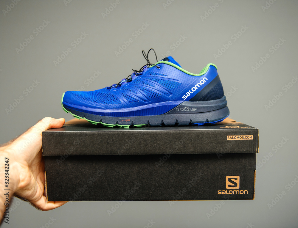 PARIS, FRANCE - NOV 22, 2018: Man holding against gray background a box  with a pair of new bluew Salomon Sense Pro Max everyday trail running  performance shoes with maximum cushioning. Stock