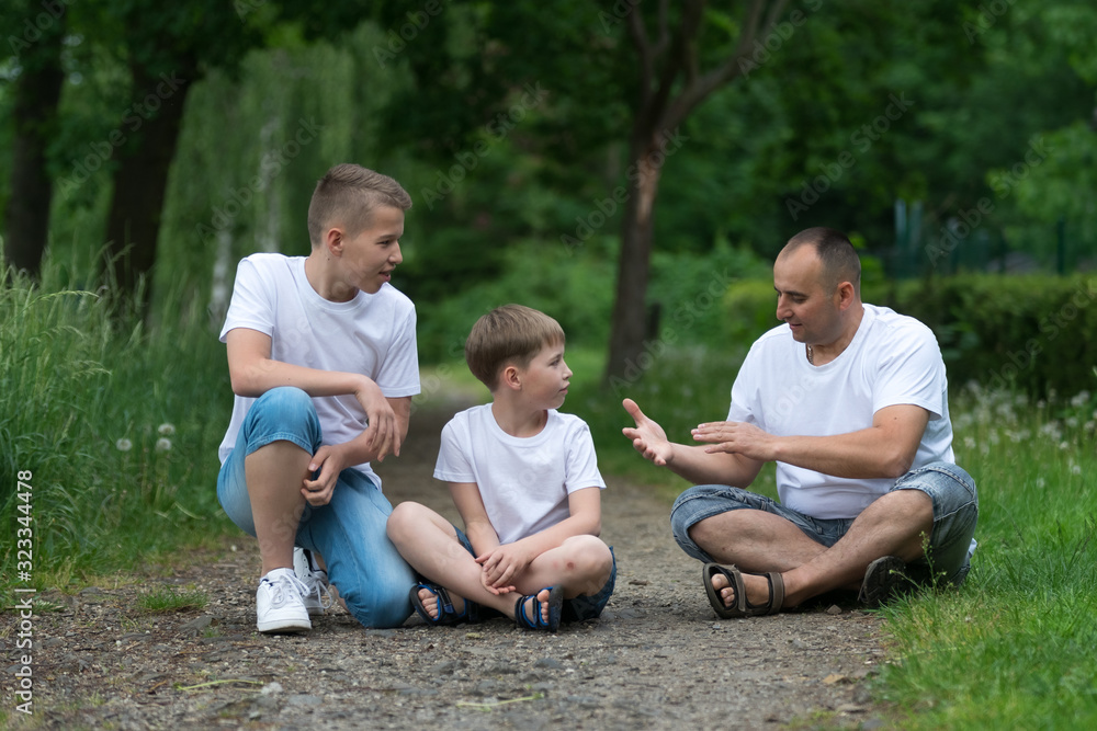 Fototapeta premium A father with his sons sits on the ground. Family portrait.