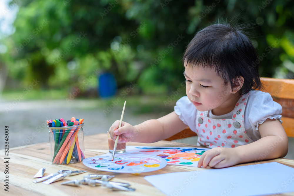 Cute little Asian girl in a white dress is drawing with painting fun Cute little Asian girl in a white dress is drawing with painting fun