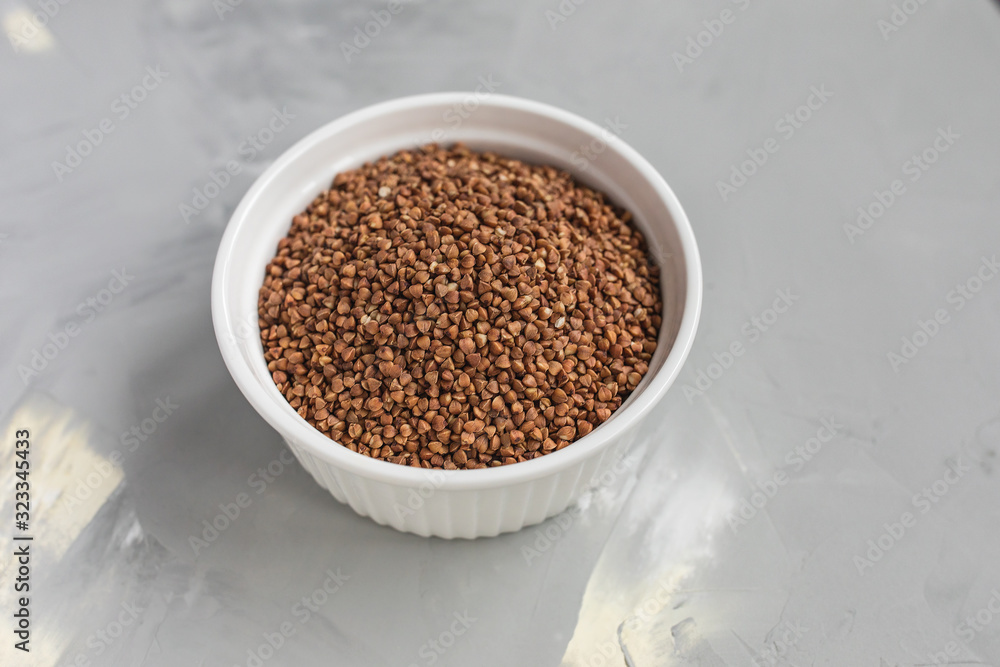 Raw buckwheat in white ceramic bowl on gray background, concept of healthy eating vegan food. Close up, selective focus, copy space Raw buckwheat in white ceramic bowl on gray background, concept of healthy eating vegan food. Close up, selective focus, copy space
