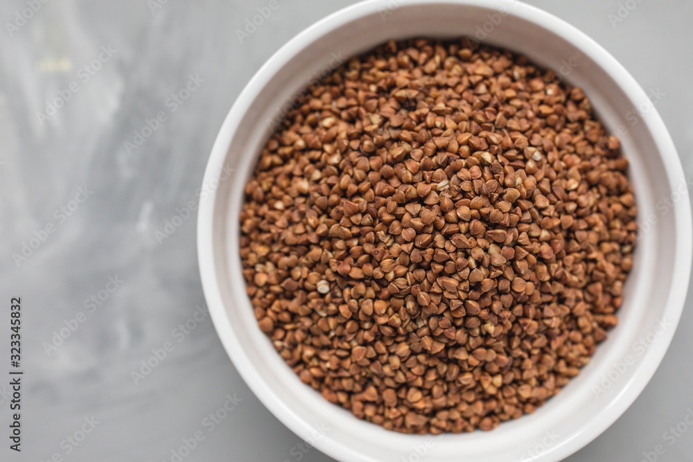 Raw buckwheat in ceramic bowl on gray background, concept of healthy eating vegan food. Close up, top view, selective focus, copy space Raw buckwheat in ceramic bowl on gray background, concept of healthy eating vegan food. Close up, top view, selective focus, copy space