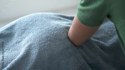 Young woman having remedial buttocks massage by young man's elbow on massage table under towel. Closeup.