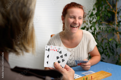 Laughing daughter playing Cribbage card game with mother at home