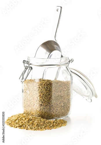 Heap of uncooked, raw freekeh or firik, roasted wheat grain, in glass storage jar with metal scoop over white photo