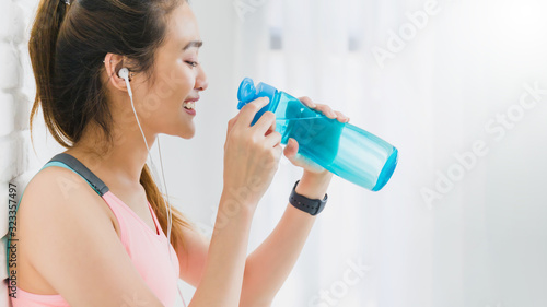 Asian beautiful woman resting and holding water bottle after play yoga and exercise on white brick wall background with copy space.Exercise for Lose weight, increase flexibility and tighten the shape.