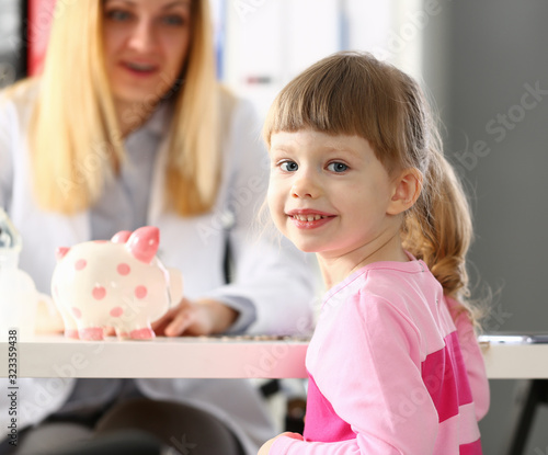 Smiling little girl at doctor office with funny piggy bank on table portrait