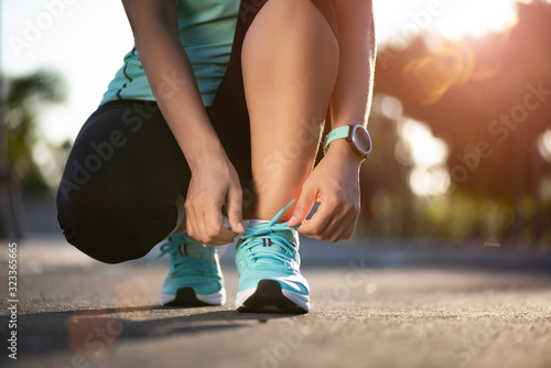 Running shoes - closeup of woman tying shoe laces. Female sport fitness runner getting ready for jogging in garden background. photo