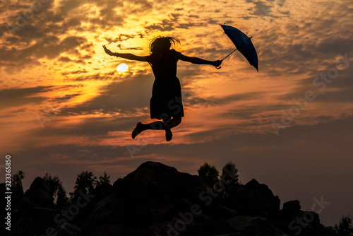 Silhouette of umbrella woman jump and sunset with big sun, landscape.