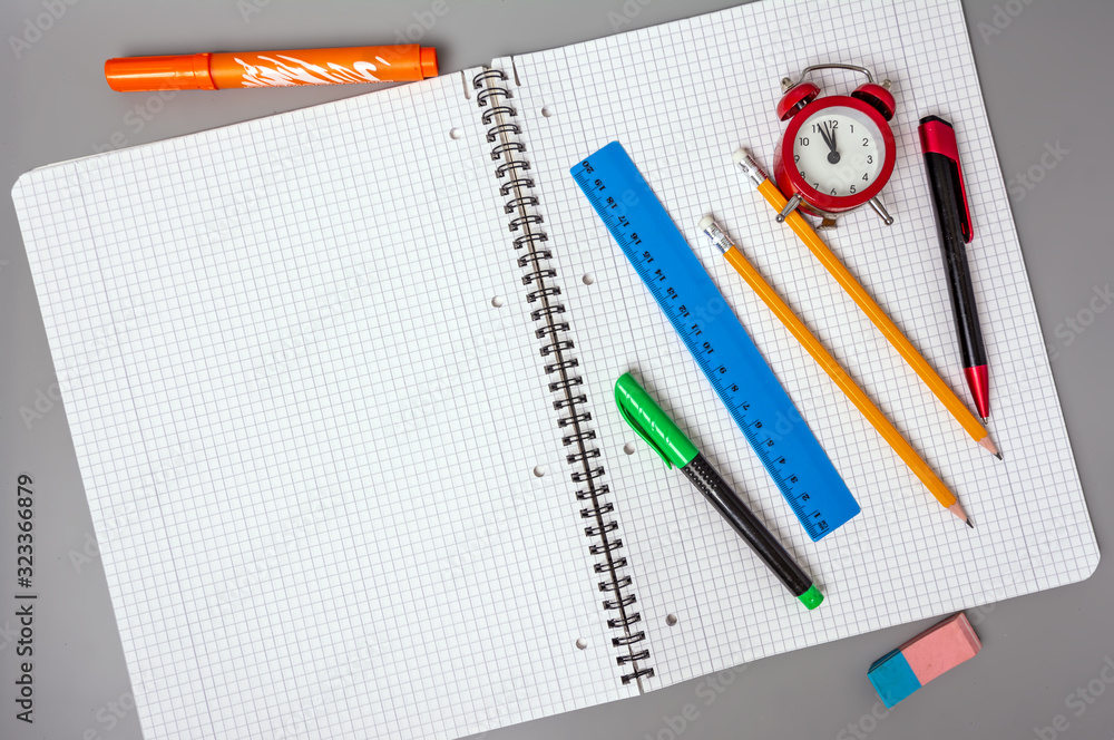 Pencils, a pen and a ruler lie on an open notebook. An alarm clock reminds of time. Office. School supplies. Pencils, a pen and a ruler lie on an open notebook. An alarm clock reminds of time. Office. School supplies.