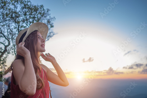 Smiling woman traveler in mountains at sunset holding hat and looking at view of nature chiangmai landmark in thailand with backpack in holiday, relaxation concept, travel concept