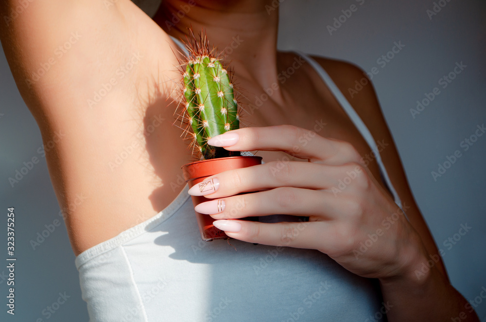 Obraz premium Woman's hand holding green cactus near her armpit,Depilation concept. Body positive concept. Concept of not shaving.