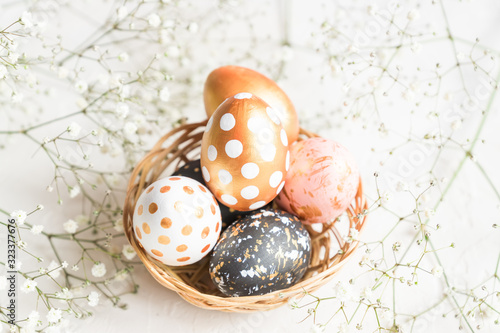 Close up of black, white and golden decorated eeaster eggs in wicker basket decorated with gypsophila on white background. photo