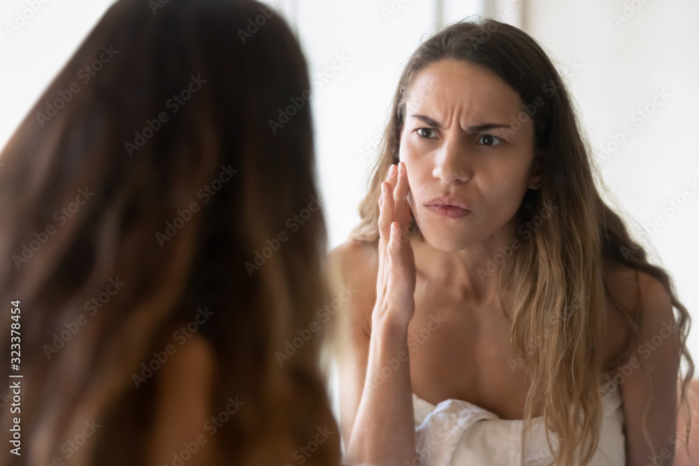 Anxious young woman look in mirror worry about skin problems Anxious young woman look in mirror worry about skin problems