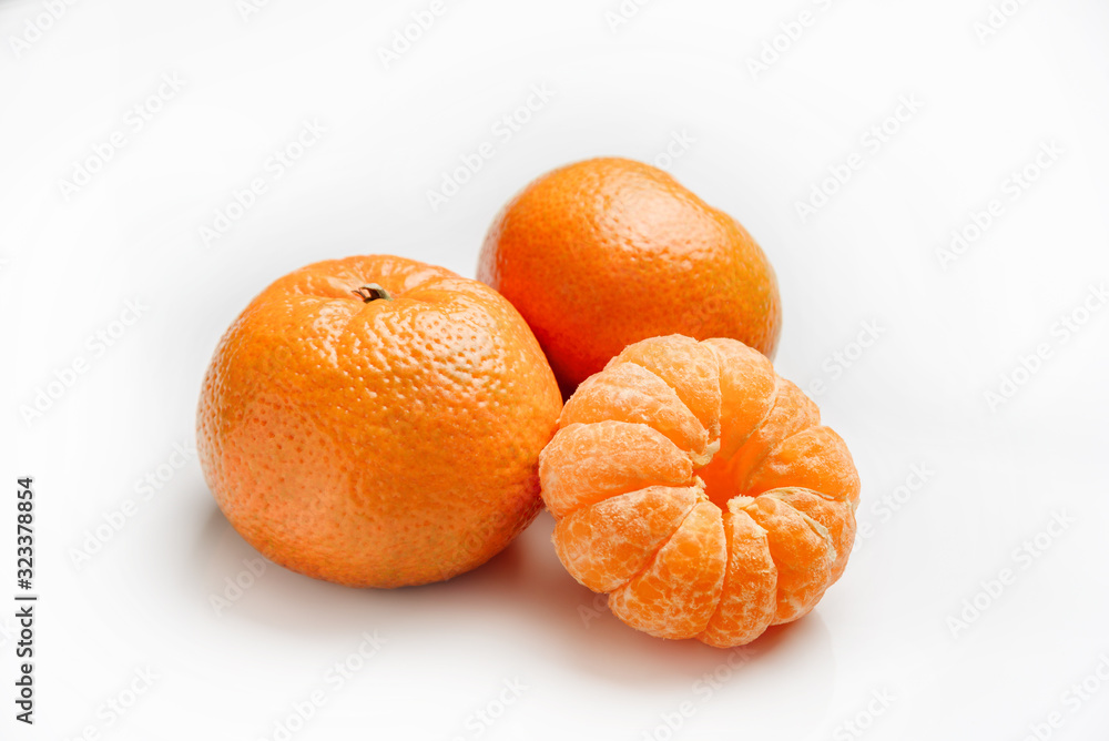 Tangerines on a white background. One peeled tangerine lies next to two tangerines in a peel. Tangerines on a white background. One peeled tangerine lies next to two tangerines in a peel.