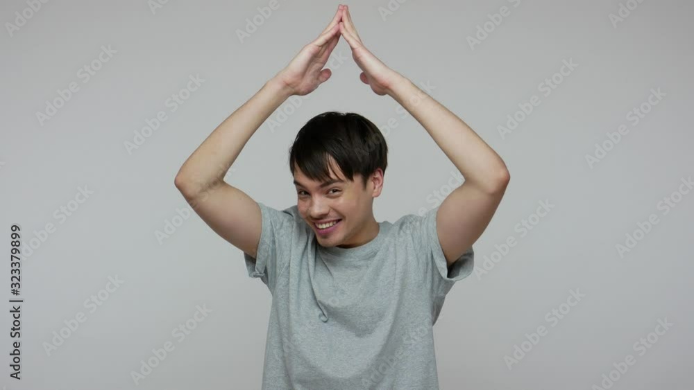 Safety at home, insurance and protected life. Funny positive excited man in T-shirt making house roof gesture with hands over head and smiling happily. indoor studio shot isolated on gray background Safety at home, insurance and protected life. Funny positive excited man in T-shirt making house roof gesture with hands over head and smiling happily. indoor studio shot isolated on gray background