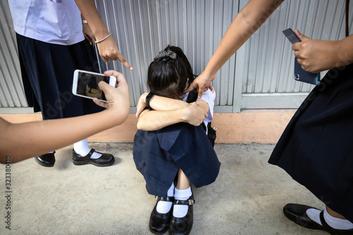 Problems of bullying at school,sad stressed asian girl student crying sitting on the floor,group of hands pointing finger to scared schoolgirl, bullying victim being video recorded on a mobile phone photo