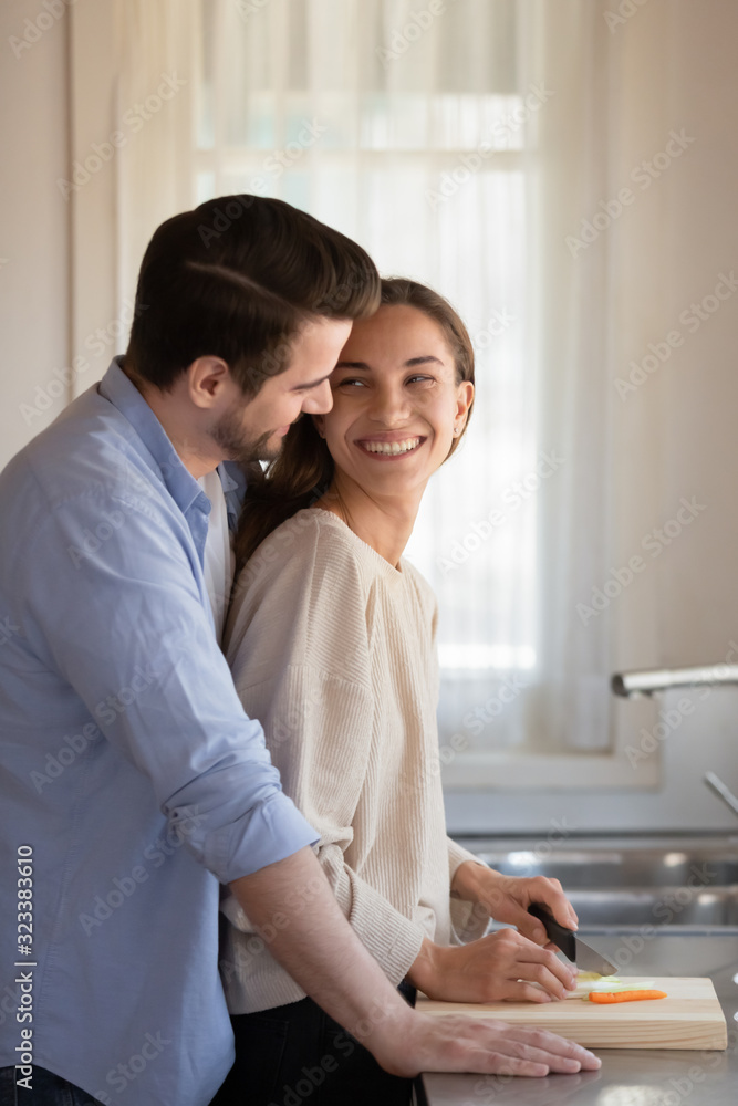 Loving newlyweds cuddle in kitchen cooking together Loving newlyweds cuddle in kitchen cooking together