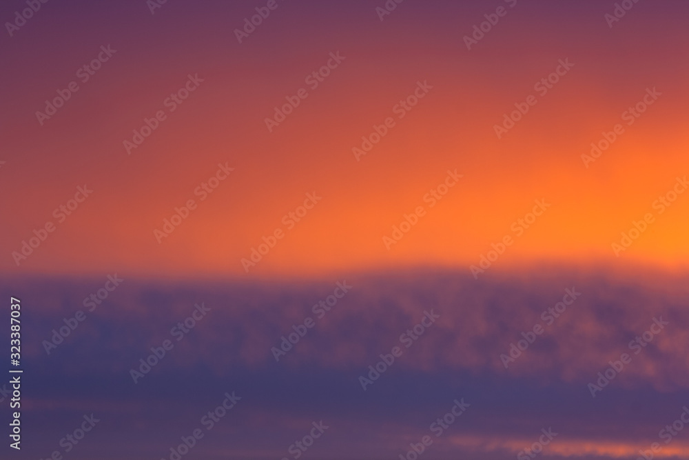 Fiery sunrise clouds in the sky. Early morning sky with colors from deep blue to orange. Sunlight in warm summer sky. Golden sunset orange yellow sky background with blue clouds