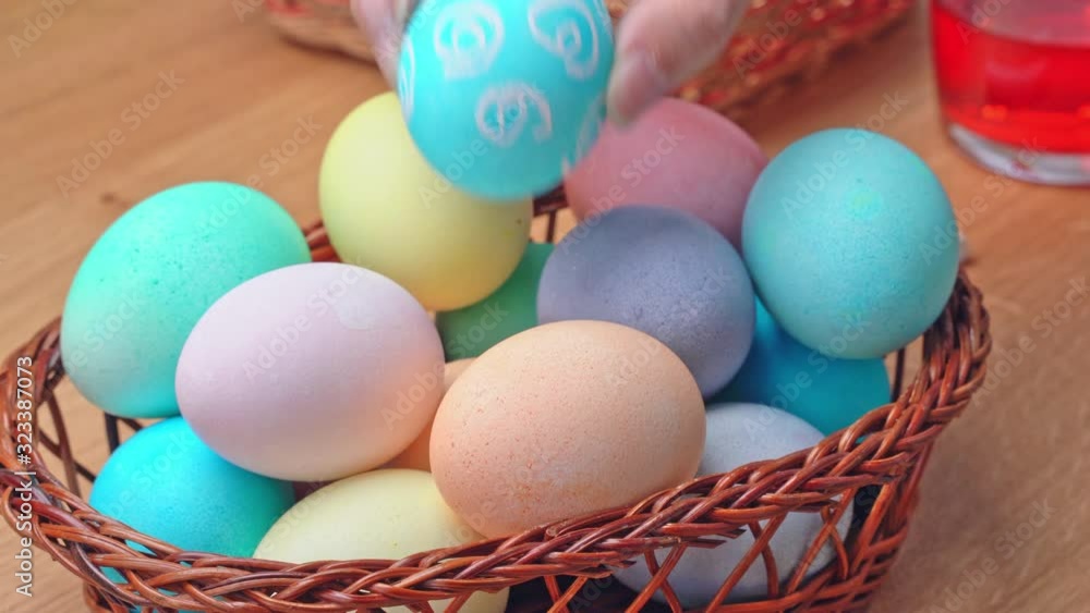 Young woman is preparing for Easter egg hunting, setting decorated colored colorful eggs in a little bamboo basket in home kitchen, close up, lifestyle, 4K. Young woman is preparing for Easter egg hunting, setting decorated colored colorful eggs in a little bamboo basket in home kitchen, close up, lifestyle, 4K.