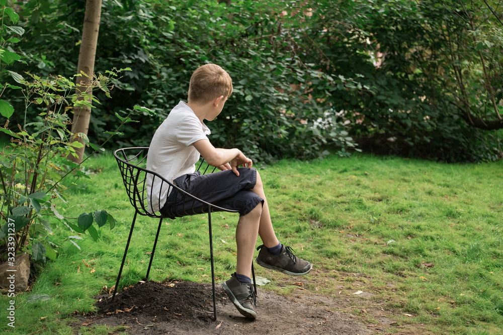 Teen boy sits alone on chair over nature background. Stay in Park. side view Teen boy sits alone on chair over nature background. Stay in Park. side view