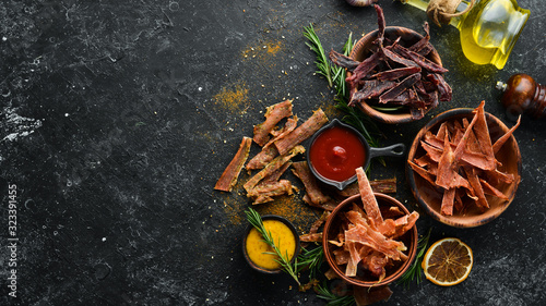 Jerky. Dried meat slices with spices and herbs. Snacks for beer On a black stone background. Top view. photo