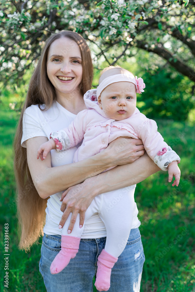 Fototapeta premium Young mother with little daughter on hands over nature background. Vertical frame
