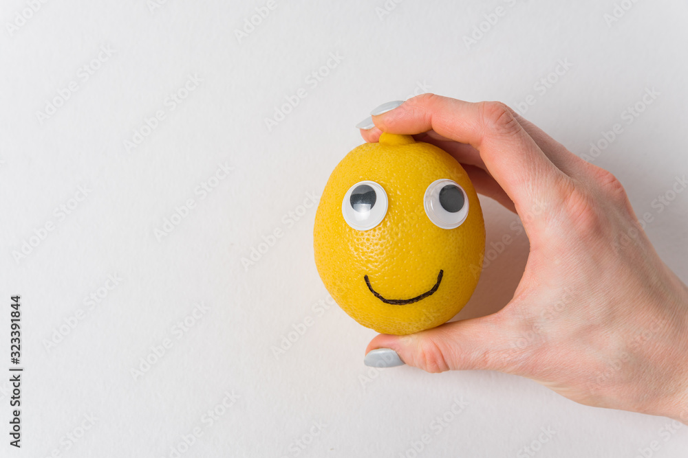 Funny lemon with eyes and smile on white background. Woman's hand holding a lemon-smile