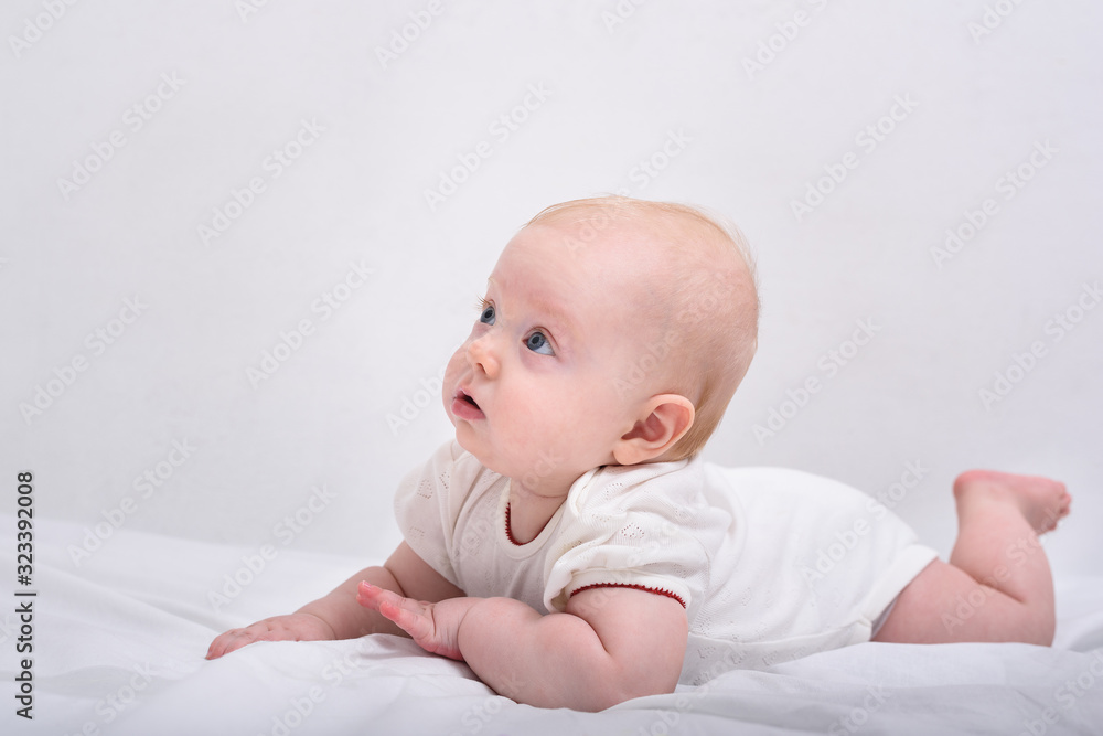 Cute and curious baby. Newborn lays on his stomach on bed. Side view