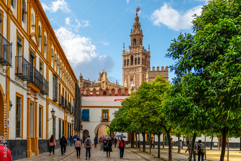 Naklejka premium Sewilla, Andaluzja, Hiszpania - 9 kwietnia 2019: Wiosenne piękno Sewilli w centrum miasta - ciepła pogoda i ludzie, majestatyczna architektura. Gotycka katedra w Sewilli. Dzwonnica La Giralda z pomnikiem El Giraldillo.