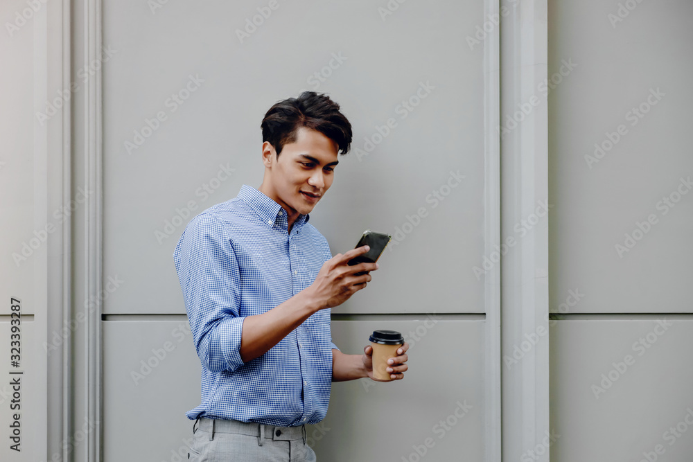 Portrait of a Happy Young Businessman Using Mobile Phone. Lifestyle of Modern People. Standing by the Wall with Coffee Cup Portrait of a Happy Young Businessman Using Mobile Phone. Lifestyle of Modern People. Standing by the Wall with Coffee Cup