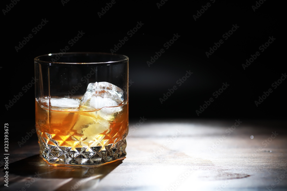 A glass of strong alcoholic drink with ice on a wooden bar counter. Whiskey with ice cubes. Glass with a chilled drink.