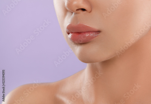 Young woman with beautiful full lips on lilac background, closeup