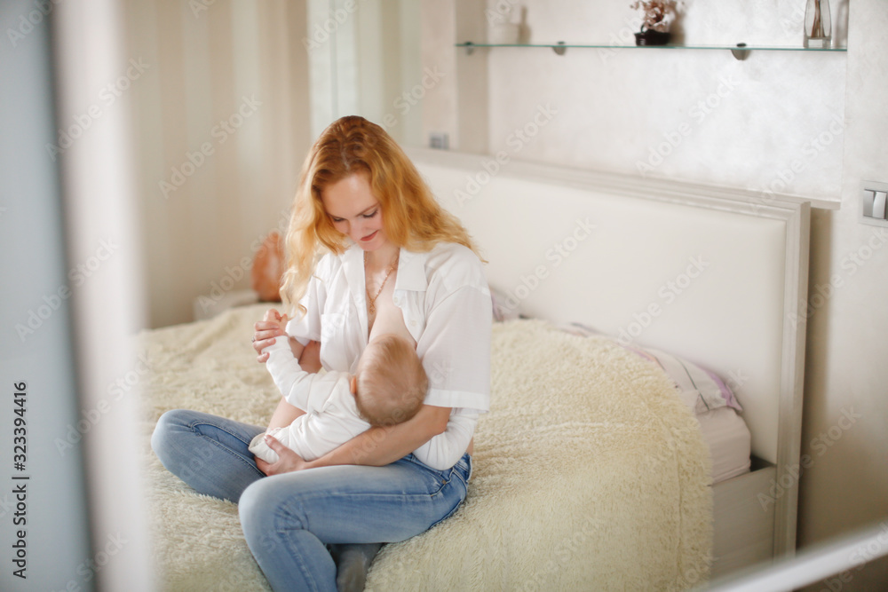 young mom blonde breastfeeds her baby in bedroom