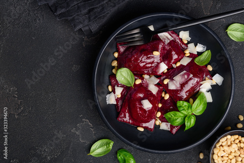 Beetroot ravioli with goat cheese, basil and pine nuts in a black plate against a dark background.  Ravioli inside with a filling of baked beets. Vegetarian food.  Space for text. Top view