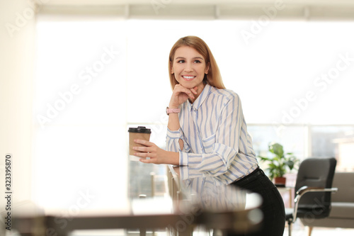 Young businesswoman with cup of coffee relaxing in office during break
