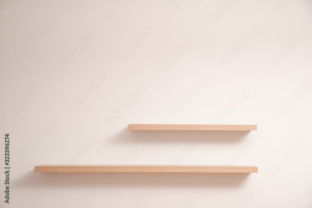 Empty stylish wooden shelves on light wall Empty stylish wooden shelves on light wall