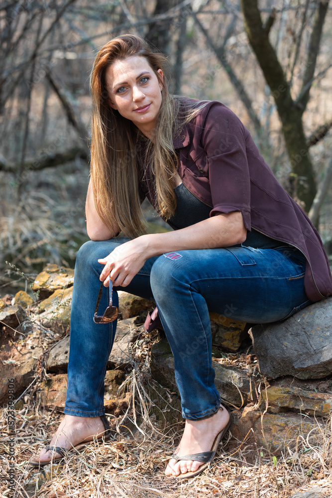 Portrait of a brunet woman with a blue denim and maroon jacket sitting rocks Portrait of a brunet woman with a blue denim and maroon jacket sitting rocks