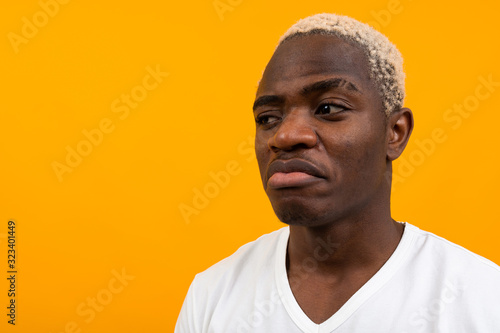 African man in a white T-shirt with a mock looks in surprise on a yellow studio background with copy space © Ivan Traimak
