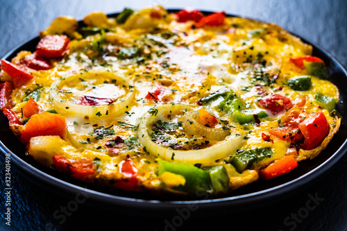 Breakfast - scrambled eggs with vegetables on black stone background