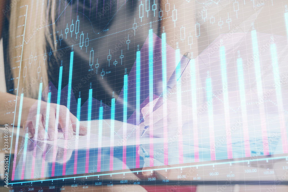 A woman hands writing information about stock market in notepad. Forex chart holograms in front. Concept of research. A woman hands writing information about stock market in notepad. Forex chart holograms in front. Concept of research.