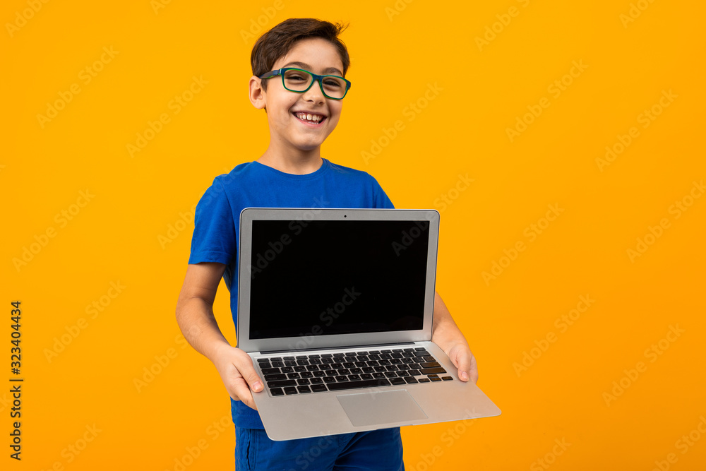 caucasian boy holds laptop screen forward with mock up on yellow studio background with copy space caucasian boy holds laptop screen forward with mock up on yellow studio background with copy space