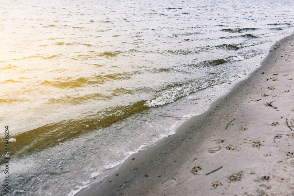 Soft wave on the sandy seashore. On the beach are traces of people and animals. Romantic landscape in the summer. Calm background. Soft wave on the sandy seashore. On the beach are traces of people and animals. Romantic landscape in the summer. Calm background.