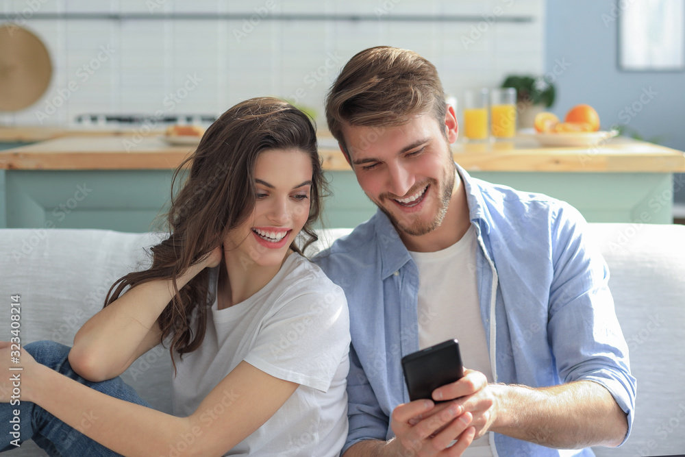 Young couple watching online content in a smart phone sitting on a sofa at home in the living room. Young couple watching online content in a smart phone sitting on a sofa at home in the living room.