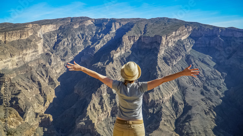 Young Foreign Female Tourist Enjoying the View of Wadi Ghul aka Grand Canyon of Oman in Jebel Shams Mountains. Woman in Active Solo Travel in Middle East Countries photo