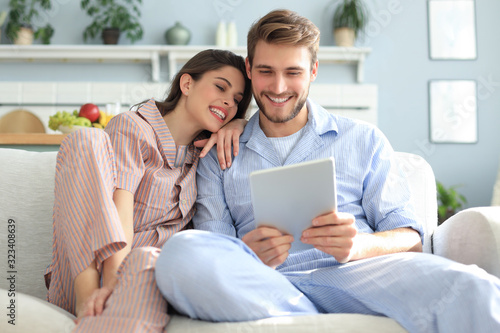 Young couple in pajamas watching media content online in a tablet sitting on a sofa in the living room.