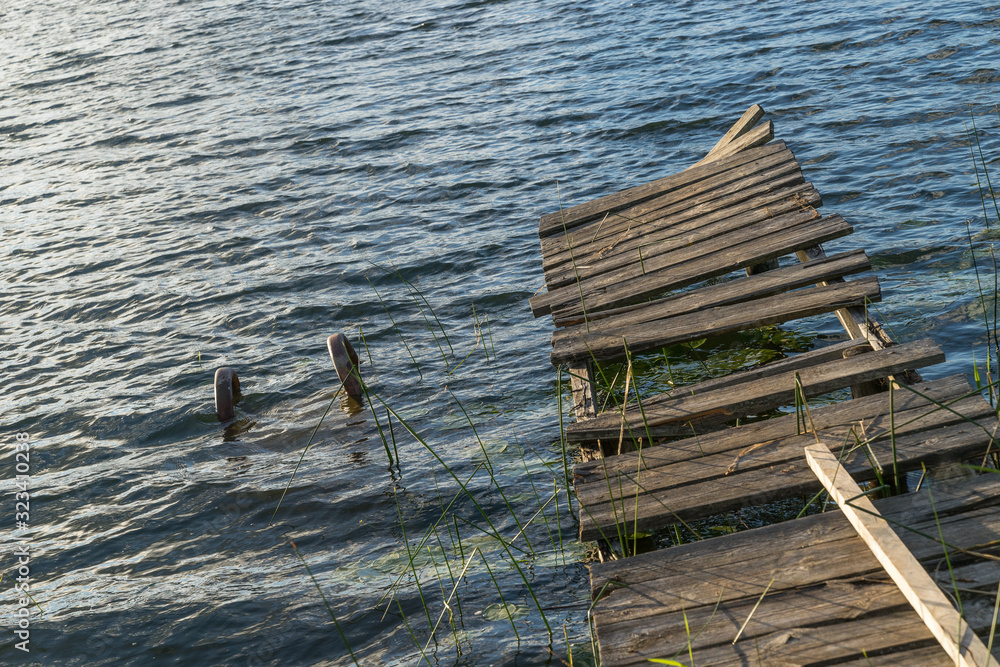 Remnants of the old abandoned wooden bridge. Desolate pier. Forest and sky reflection on water. Shore of a single lake Remnants of the old abandoned wooden bridge. Desolate pier. Forest and sky reflection on water. Shore of a single lake